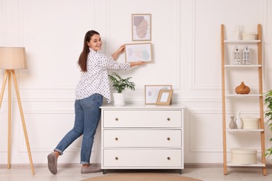 Woman hanging picture frame on white wall at home