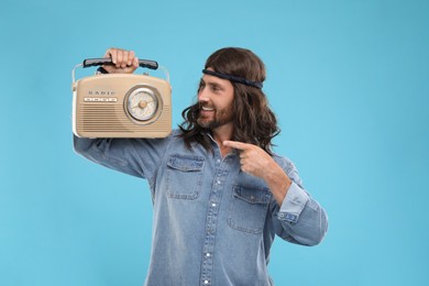 Photo of Stylish hippie man pointing at retro radio receiver on light blue background