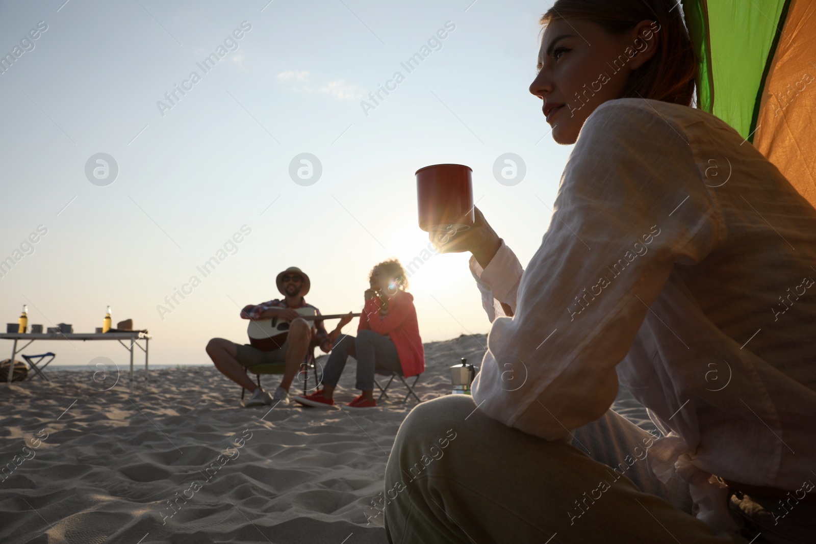 Photo of Friends resting on sandy beach. View from camping tent