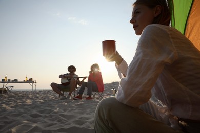 Photo of Friends resting on sandy beach. View from camping tent