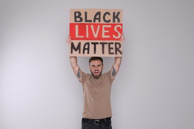 Photo of Emotional young man holding sign with phrase Black Lives Matter on light background. End racism