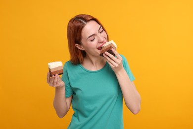 Young woman eating pieces of tasty cake on orange background