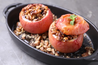 Tasty baked apples with nuts, honey and mint in baking dish on gray table, closeup