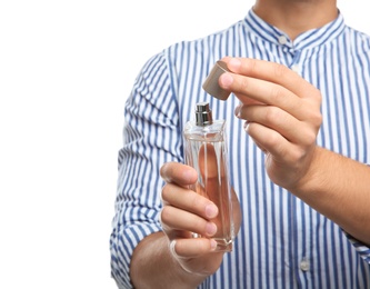 Young man holding bottle of perfume on white background, closeup
