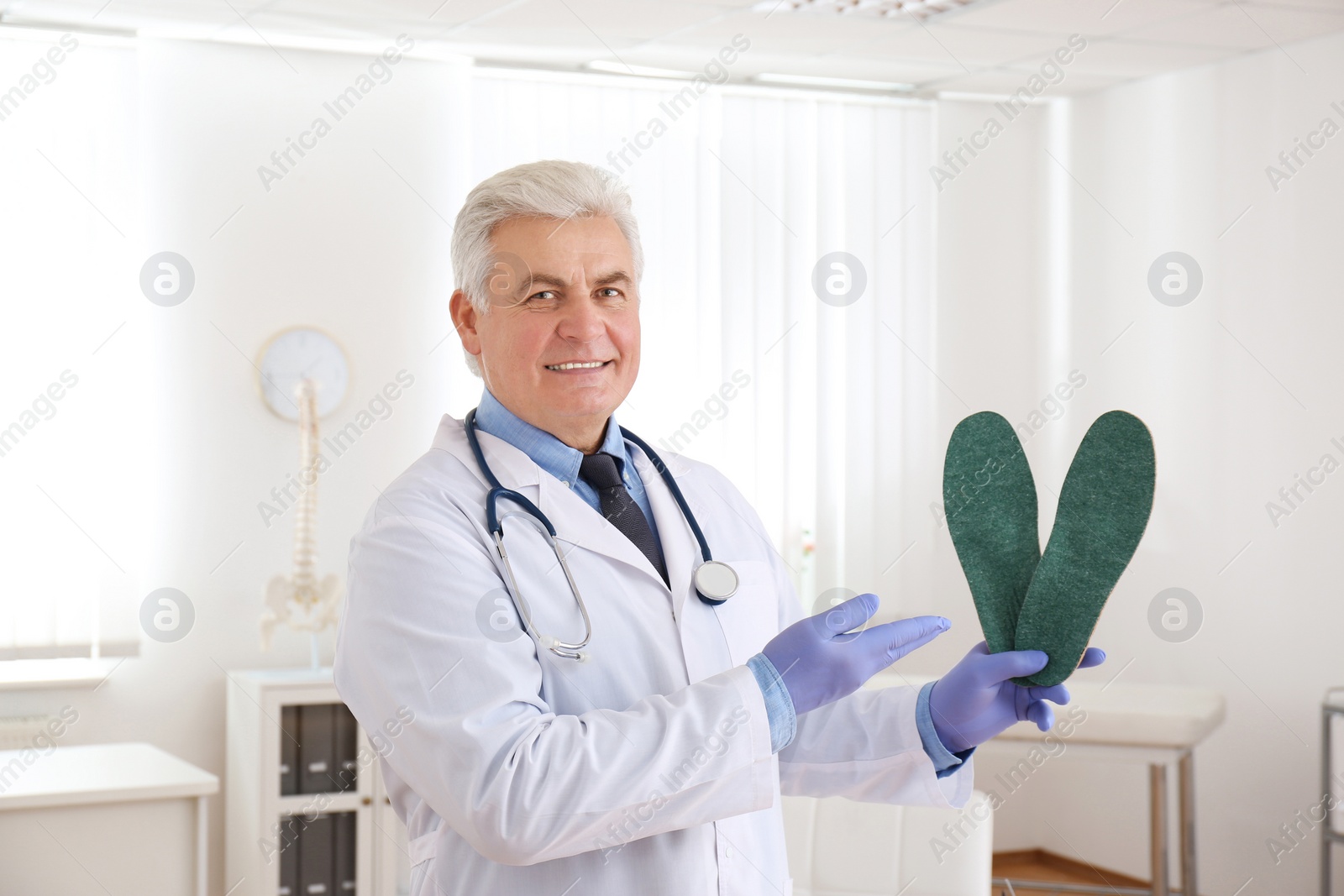 Photo of Senior male orthopedist showing insoles in clinic