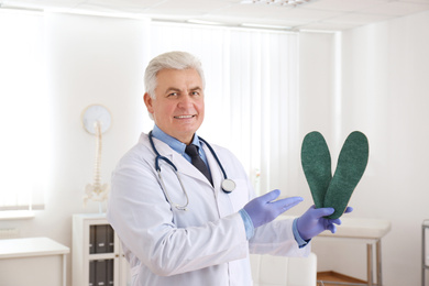 Senior male orthopedist showing insoles in clinic