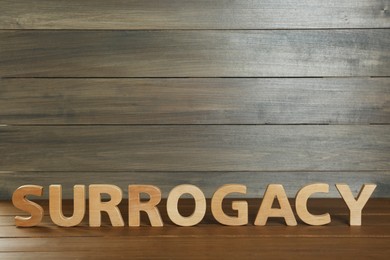 Photo of Word Surrogacy made of wooden letters on table, space for text