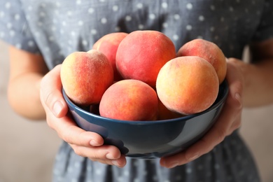 Photo of Woman holding bowl with delicious ripe peaches, closeup