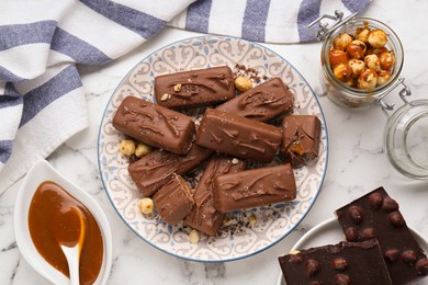 Photo of Delicious chocolate candy bars, caramel and nuts on white marble table, flat lay