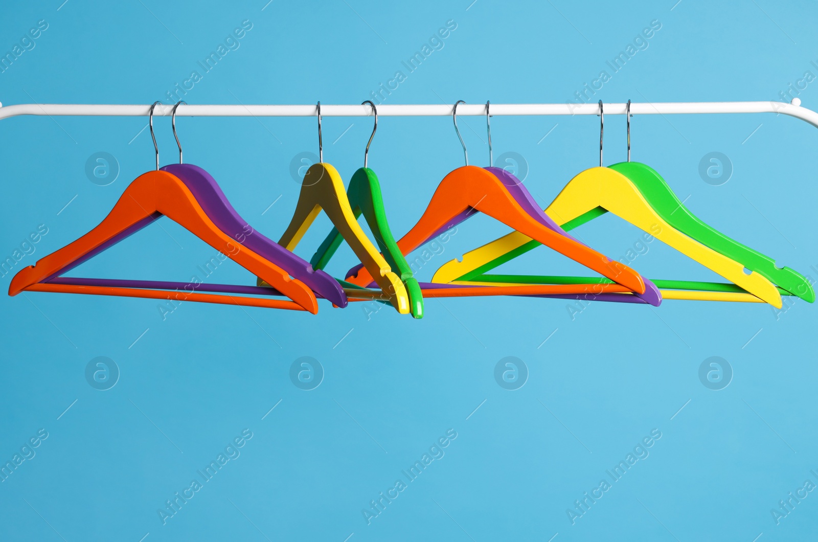 Photo of Bright clothes hangers on metal rail against light blue background