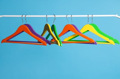 Photo of Bright clothes hangers on metal rail against light blue background