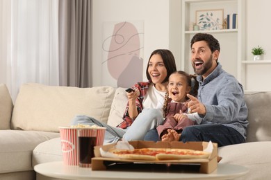 Photo of Excited family watching TV with popcorn and pizza on sofa at home, space for text