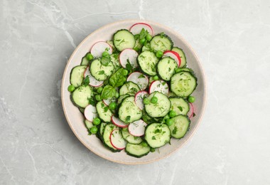 Photo of Appetizing salad with cucumbers, radish and pea in bowl on light grey table, top view