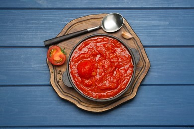 Photo of Homemade tomato sauce in bowl, spoon and ingredients on blue wooden table, top view