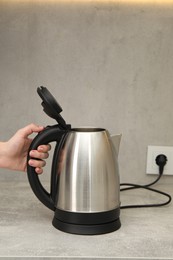 Photo of Woman with electric kettle in kitchen, closeup