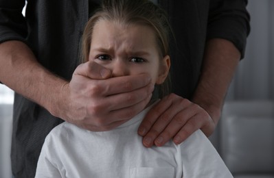 Photo of Man covering scared little girl's mouth indoors. Domestic violence