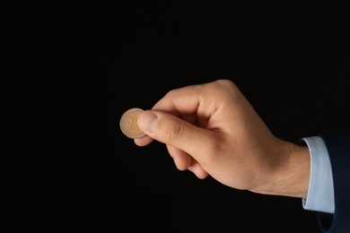 Young man holding coin on black background, closeup