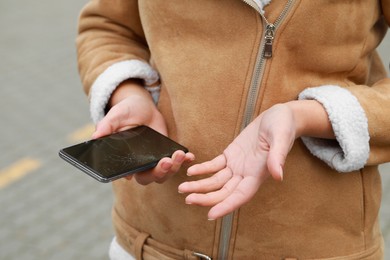 Woman holding damaged smartphone outdoors, closeup. Device repairing