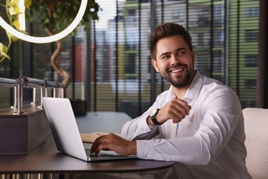 Photo of Happy young man working on laptop at table in office