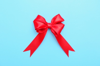 Red ribbon bow on color background, top view