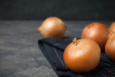 Photo of Black fabric with ripe onions on grey table, space for text