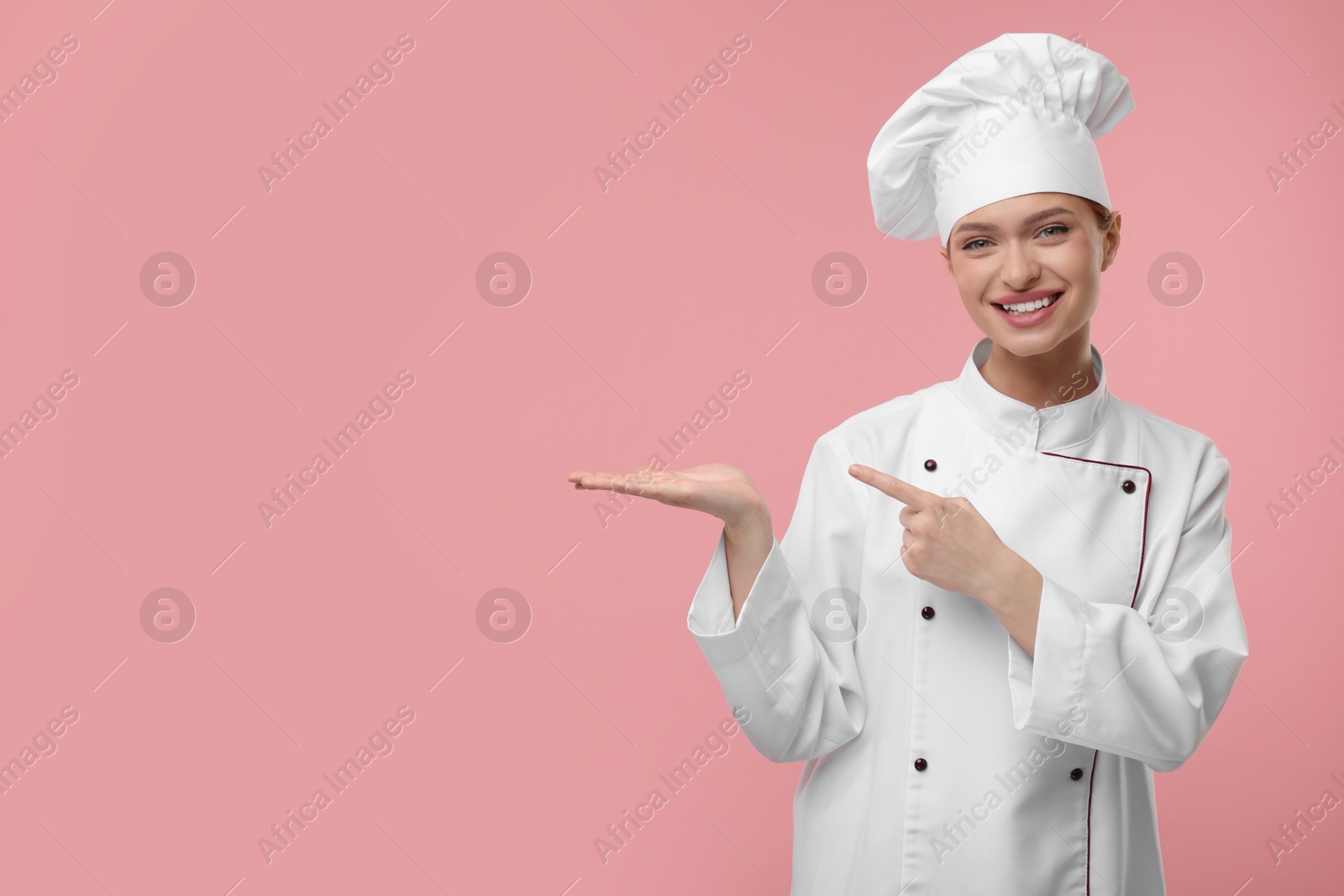 Photo of Happy chef in uniform pointing at something on pink background, space for text