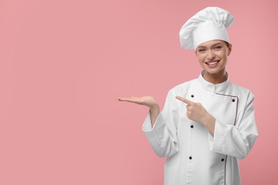 Photo of Happy chef in uniform pointing at something on pink background, space for text