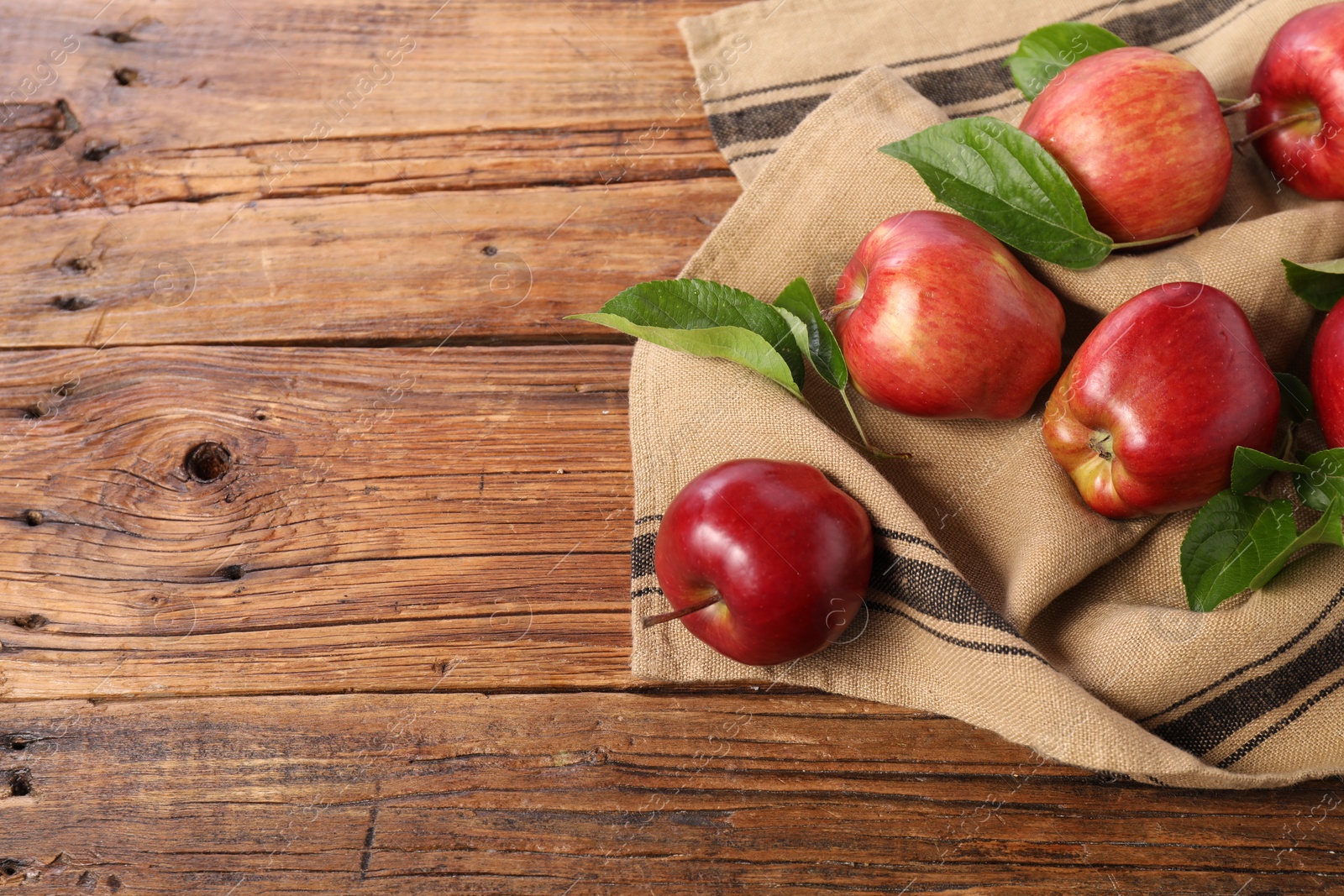 Photo of Ripe red apples with leaves on wooden table. Space for text