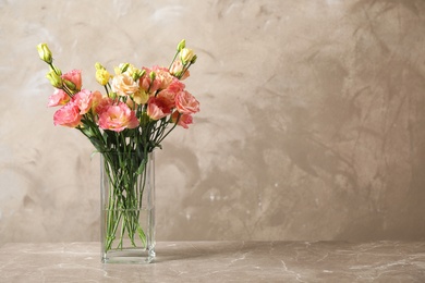 Photo of Eustoma flowers in vase on table near beige wall, space for text