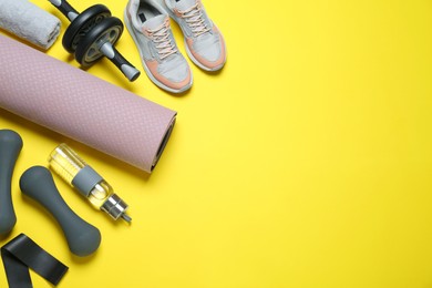 Photo of Exercise mat, dumbbells, bottle of water, ab roller, fitness elastic band, towel and shoes on yellow background, flat lay. Space for text
