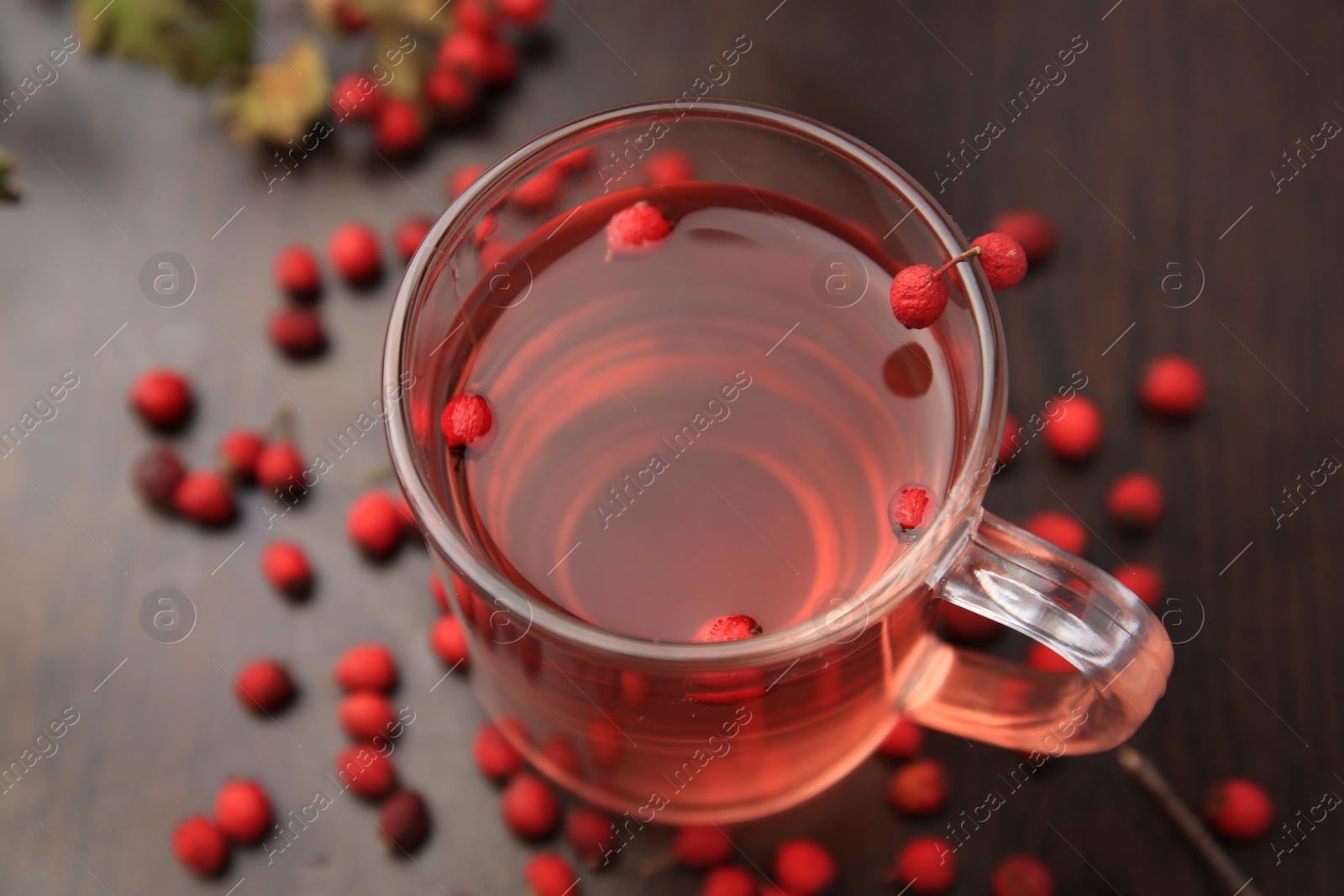 Photo of Cup with hawthorn tea and berries on wooden table, above view