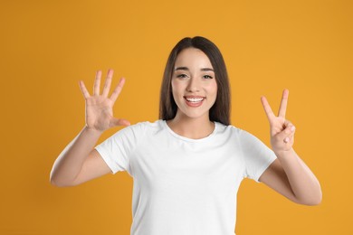 Woman in white t-shirt showing number seven with her hands on yellow background