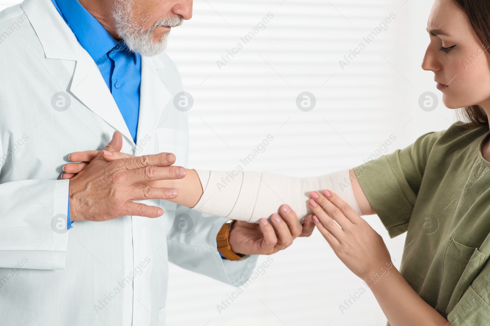 Photo of Orthopedist applying bandage onto patient's elbow in clinic, closeup
