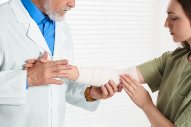 Orthopedist applying bandage onto patient's elbow in clinic, closeup