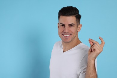 Handsome man snapping fingers on light blue background. Space for text
