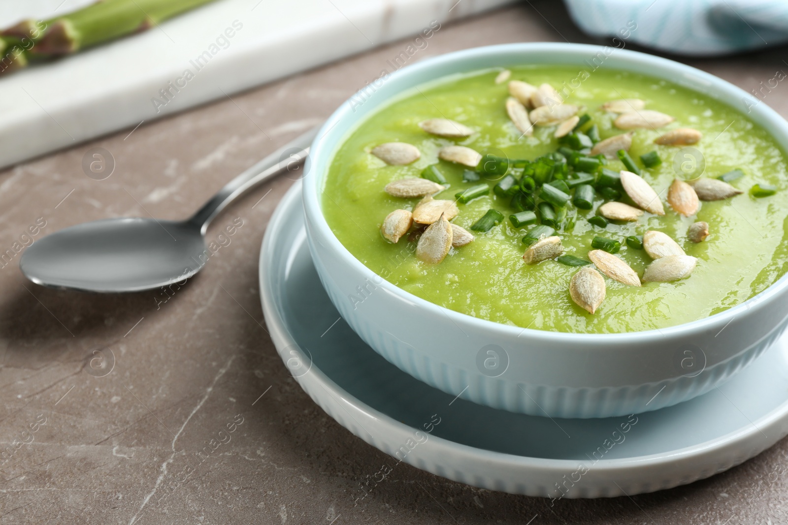 Photo of Delicious asparagus soup in bowl on grey marble table