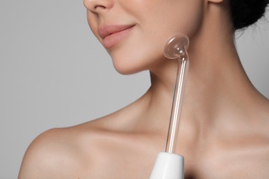 Photo of Woman using high frequency darsonval device on grey background, closeup