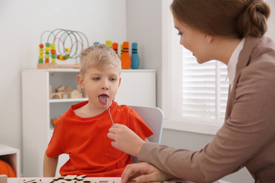 Photo of Speech therapist using logopedic probe during session with little boy in office