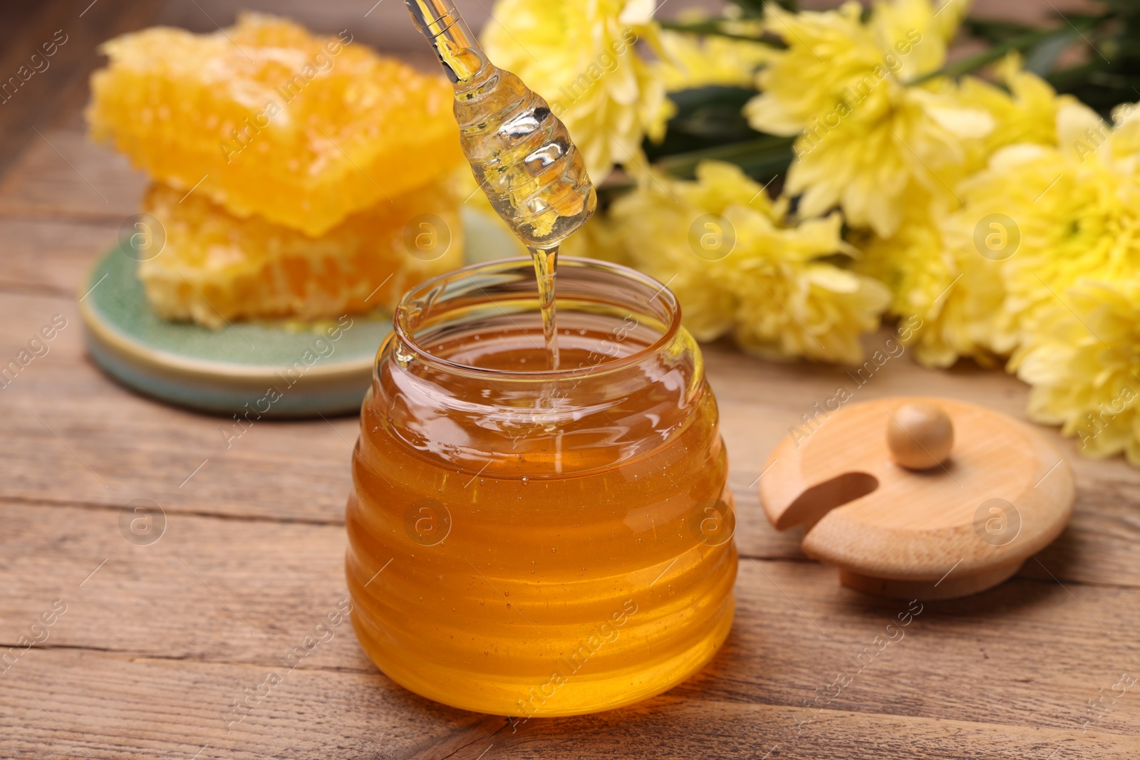 Photo of Pouring sweet golden honey from dipper into jar at wooden table, closeup