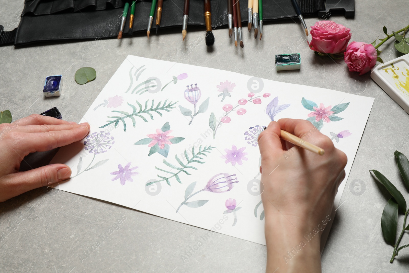 Photo of Woman painting flowers with watercolor at grey stone table, closeup