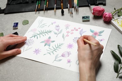 Photo of Woman painting flowers with watercolor at grey stone table, closeup