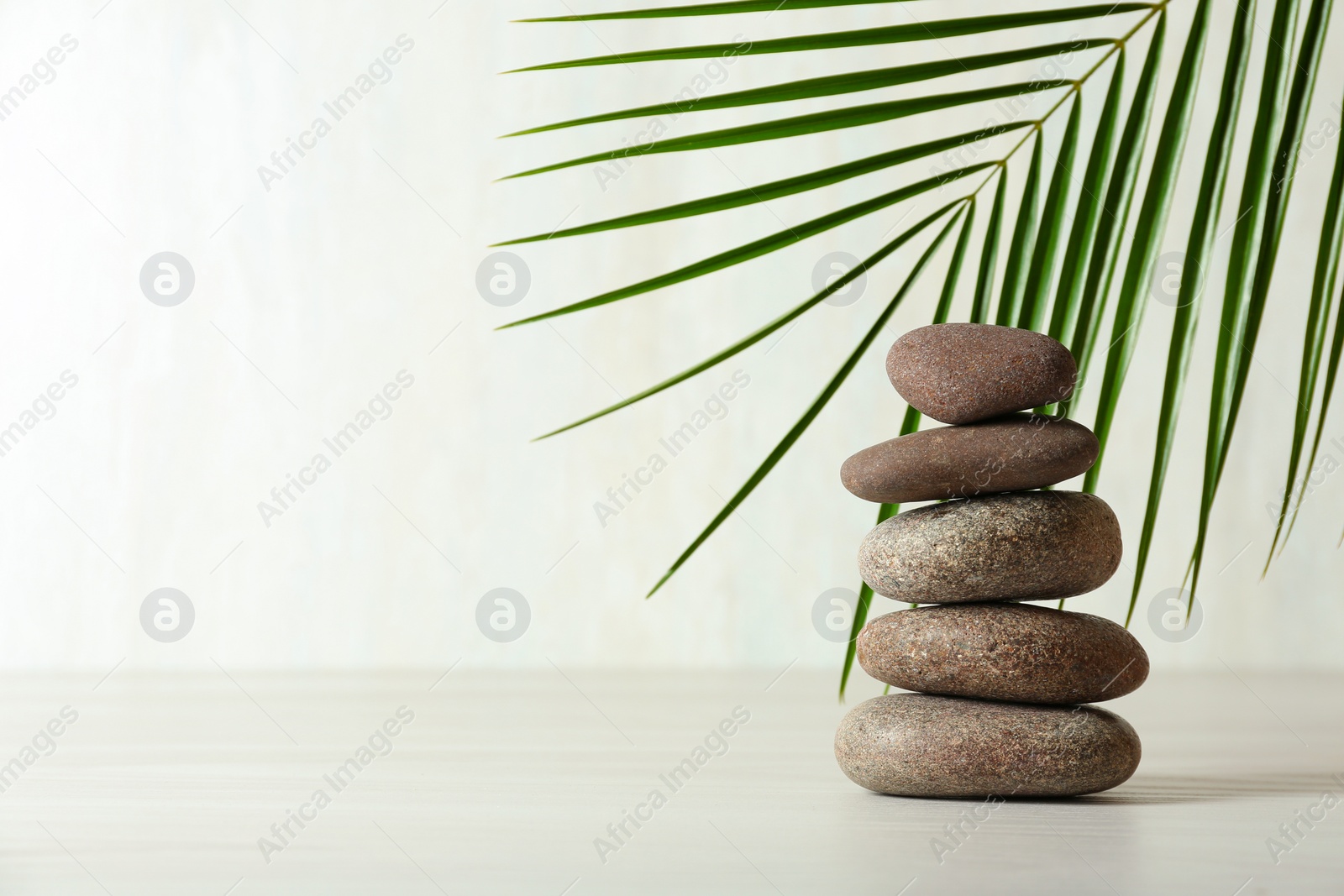 Photo of Stack of spa stones and palm leaf on table against white background, space for text