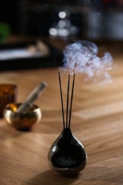 Photo of Incense sticks smoldering in holder on wooden table indoors