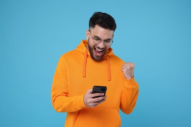 Photo of Happy young man using smartphone on light blue background