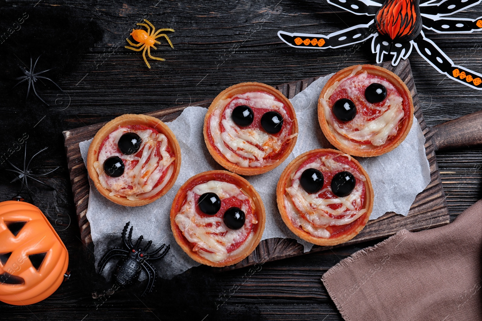 Photo of Cute monster tartlets served on black wooden table, flat lay. Halloween party food