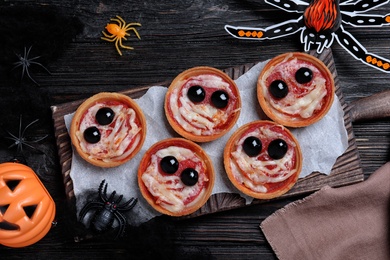 Cute monster tartlets served on black wooden table, flat lay. Halloween party food