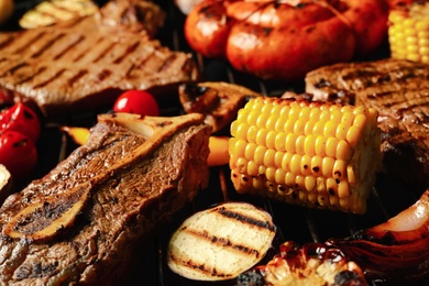 Photo of Fresh grilled meat steaks and vegetables on barbecue grate, closeup