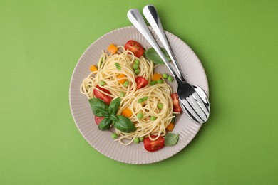 Photo of Plate of delicious pasta primavera and cutlery on light green background, top view