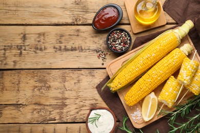 Tasty cooked corn cobs and products on wooden table, flat lay, Space for text