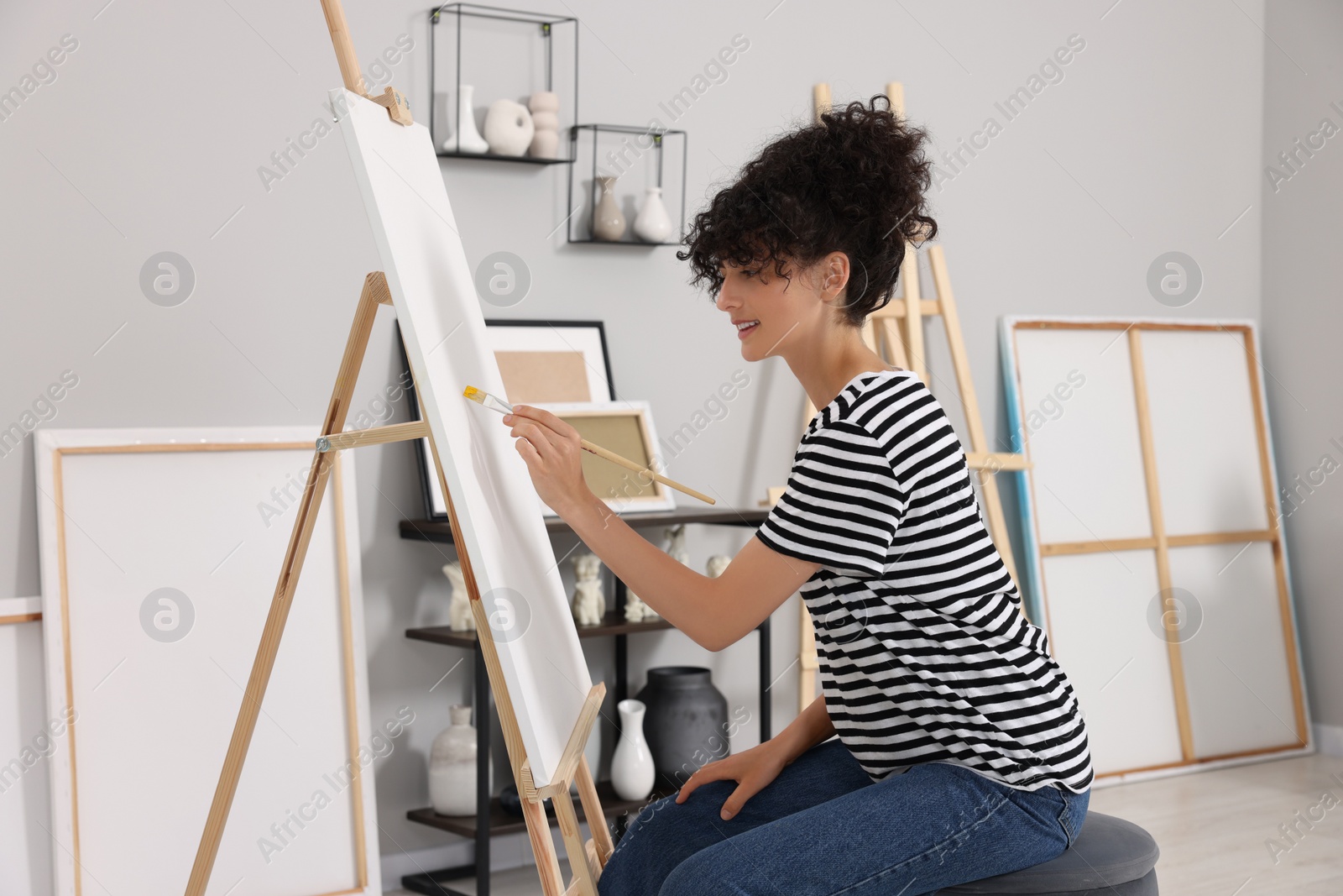 Photo of Young woman painting on easel with canvas in studio